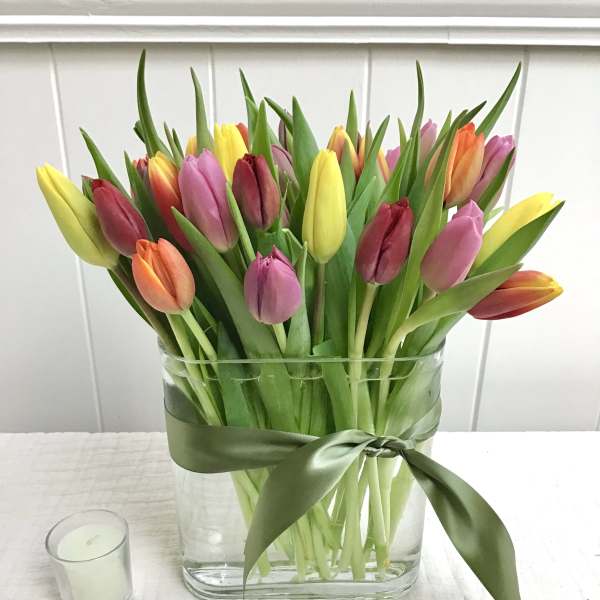 Colorful tulips arranged in a clear glass vase with a green ribbon