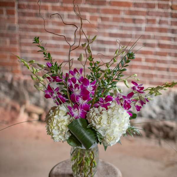 Tall vase arrangement with purple orchids and white hydrangeas