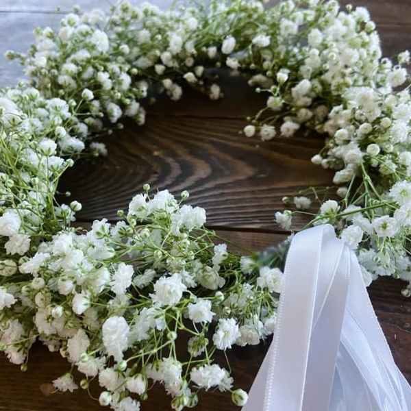 White baby's breath wreath with a white ribbon on a wooden surface