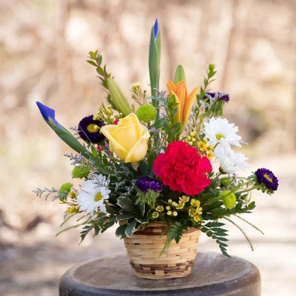 Mixed flower arrangement in a woven basket with daisies and roses