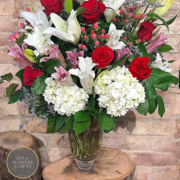 Tall bouquet of red roses, white and pink lilies, and white hydrangeas in a clear glass vase