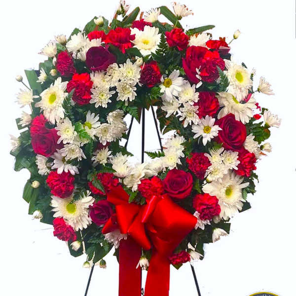 Standing wreath of red roses, red carnations, and white daisies with a red bow.