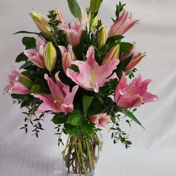 Pink lilies arranged in a clear glass vase with greenery