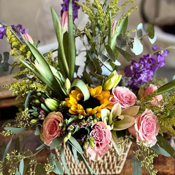 Mixed flower arrangement in a woven basket with pink roses and a sunflower