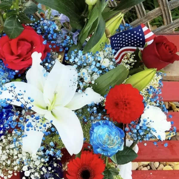 Red, white, and blue floral arrangement with lilies, roses, and small flags