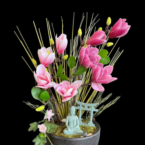 Pink magnolia-like flowers in a black pot with a small Buddha figurine