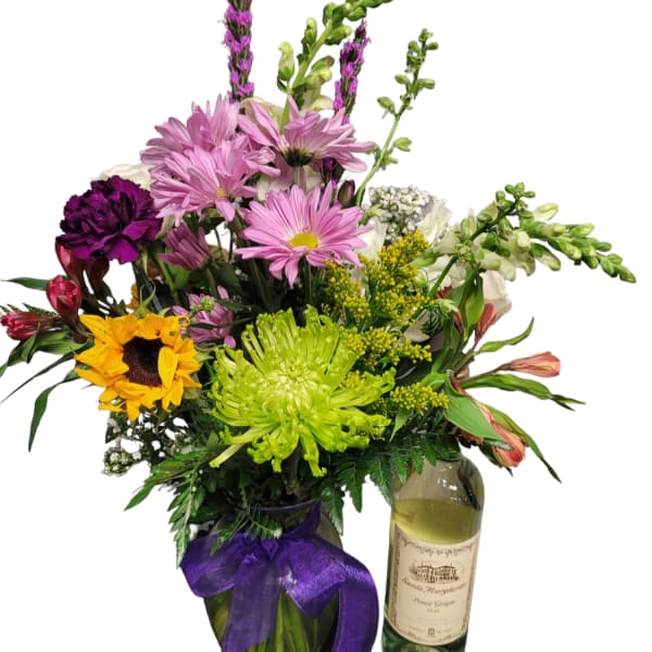 Mixed bouquet in a glass vase beside a wine bottle