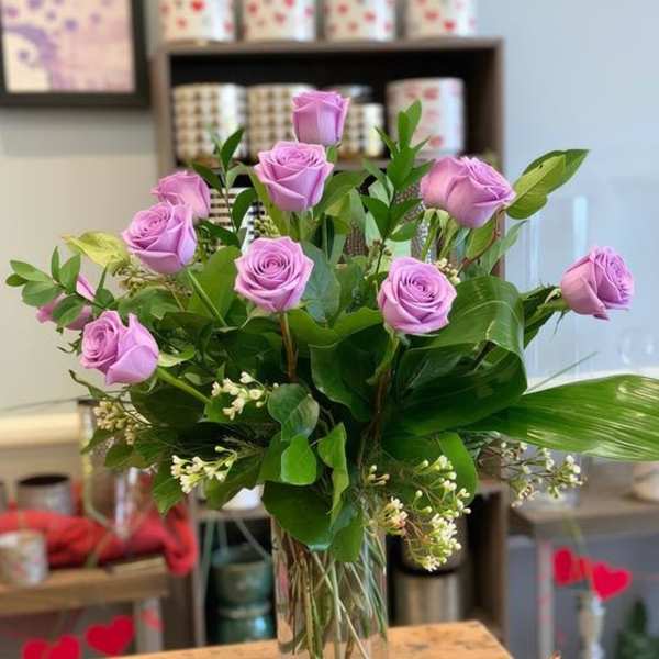 Lavender roses arranged in a clear glass vase with greenery