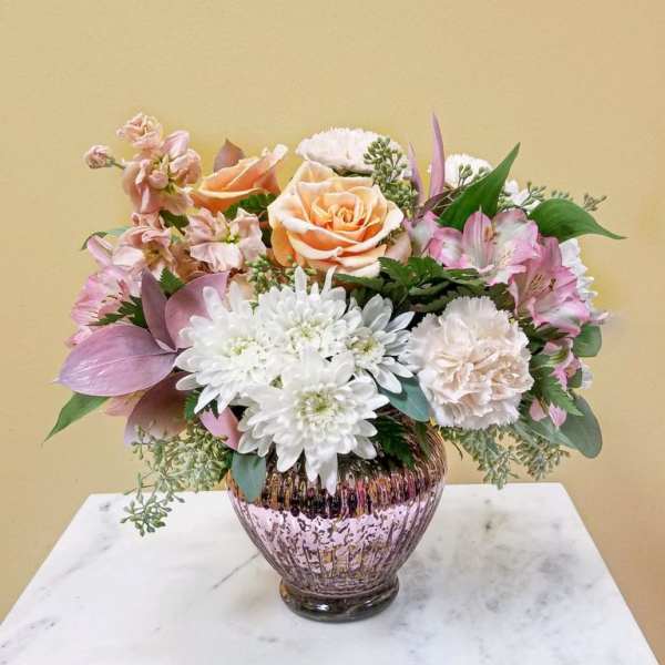 Mixed bouquet of peach, pink, and white flowers in a pink glass vase