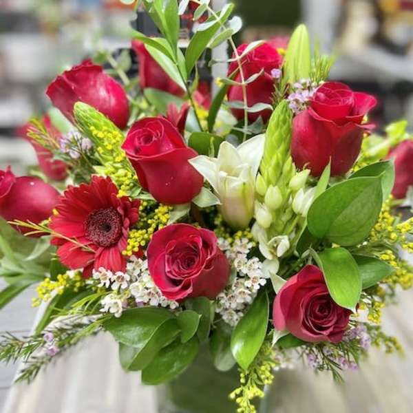 Red rose and white lily arrangement with accent blooms in a clear glass cube vase