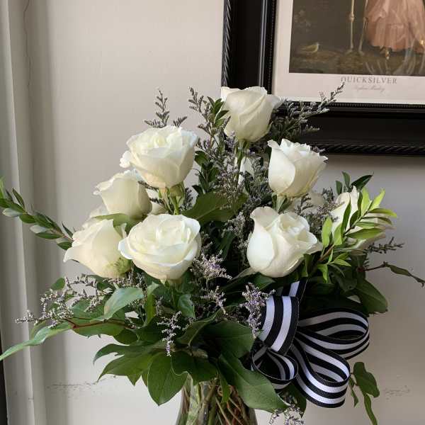 White roses arranged in a glass vase with a black-and-white ribbon