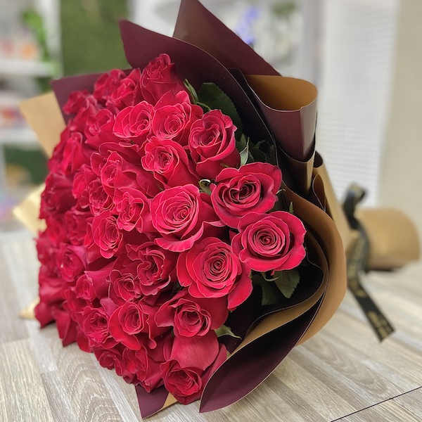 Large bouquet of red roses wrapped in brown and burgundy paper on a table