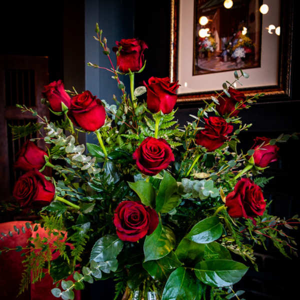 Red roses arranged in a clear glass vase with mixed greenery