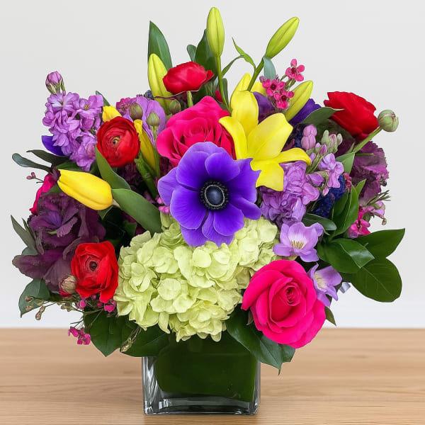Colorful bouquet in a square glass vase with roses, lilies, and purple blooms