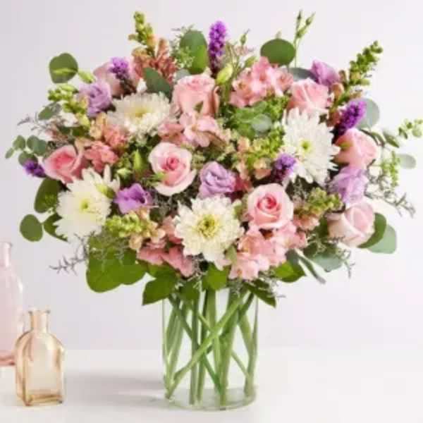 Large pastel arrangement of pink roses, white mums, and lavender blooms in a clear glass vase