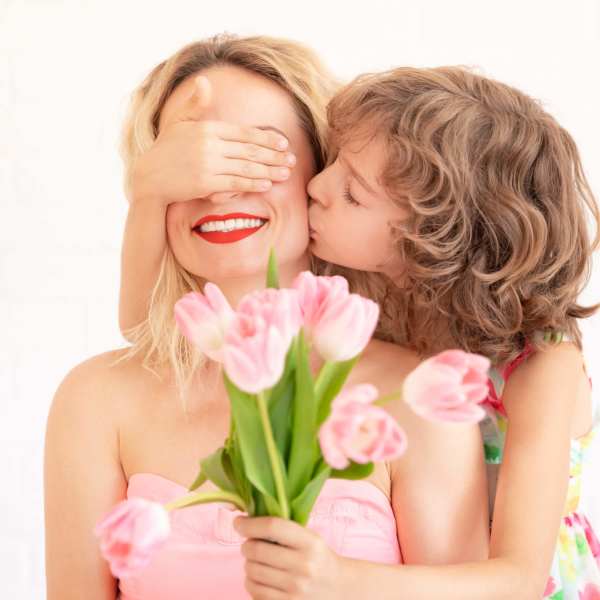 Woman holding pink tulips while a child kisses her cheek