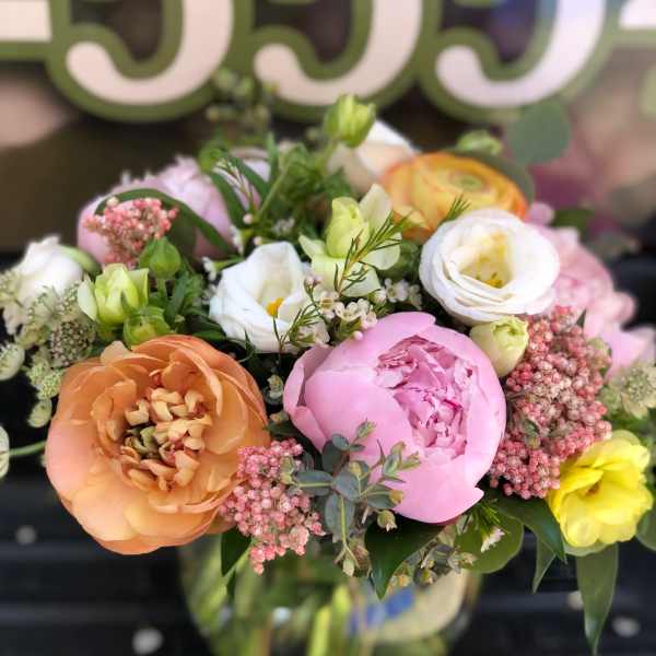Mixed pastel bouquet with peonies, ranunculus, and small blooms in a glass vase