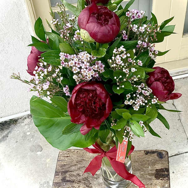 Bouquet of deep red peonies with pink filler flowers in a glass vase