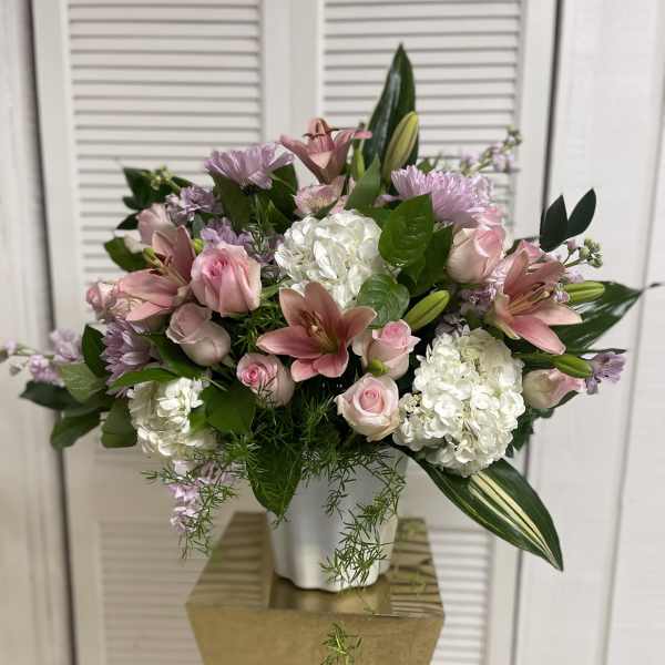 Pink lilies and roses arranged with white hydrangeas in a white vase