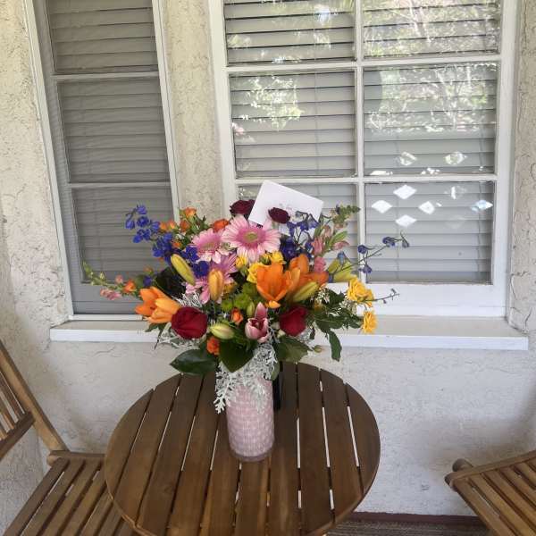 Colorful mixed flower bouquet in a pink vase on a patio table