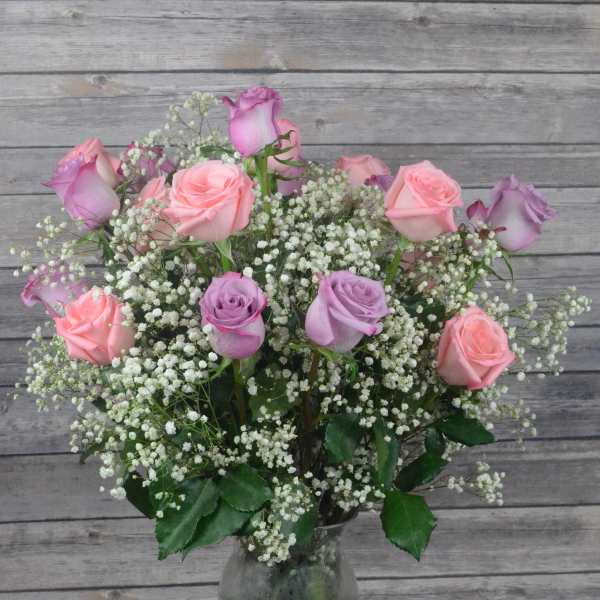 Pink and lavender roses in a clear glass vase with baby's breath