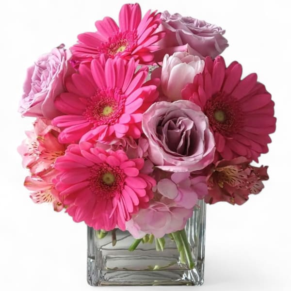Pink gerbera daisies and roses arranged in a clear square vase