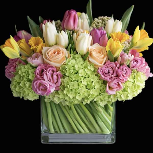 Mixed bouquet of tulips, roses, and hydrangeas in a clear glass vase
