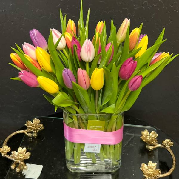 Colorful tulips arranged in a clear glass vase with a pink ribbon