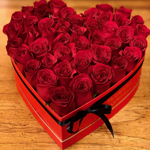 Heart-shaped box filled with red roses and tied with a black ribbon
