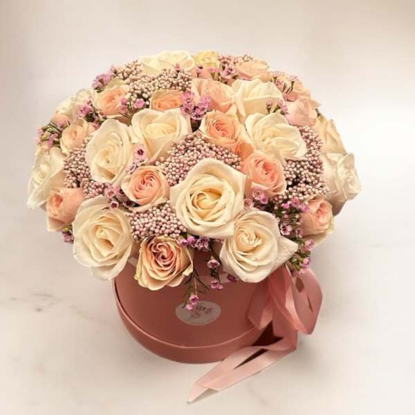 Cream and blush roses arranged in a pink round box with a ribbon