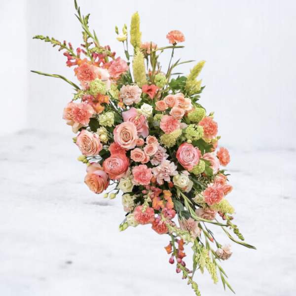 Asymmetrical cascading arrangement of peach and pink roses and carnations with light green accent blooms.