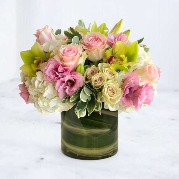 Low arrangement of pink roses, green orchids, and white hydrangeas in a green glass cylinder vase