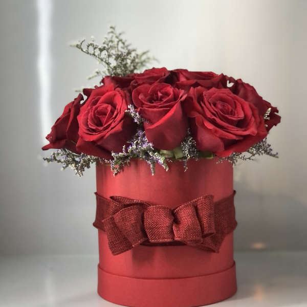 Red roses arranged in a round red box with a ribbon bow