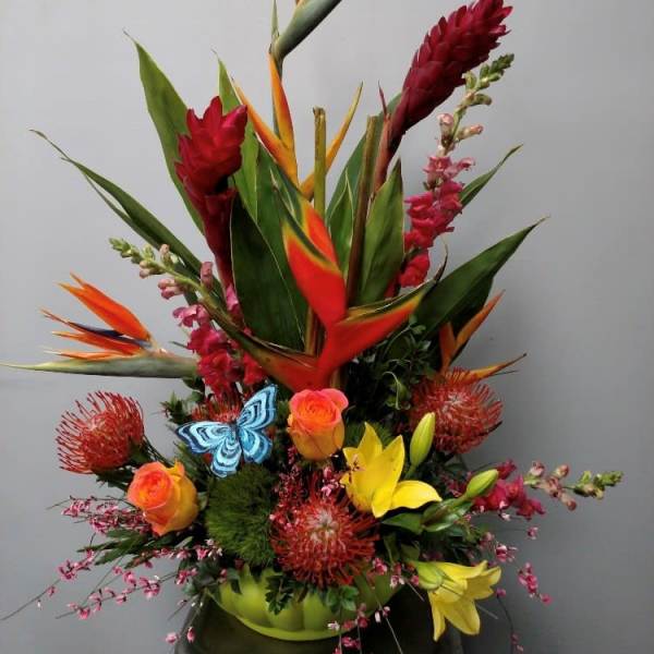 Tropical flower arrangement with orange bird-of-paradise and red blooms in a green container