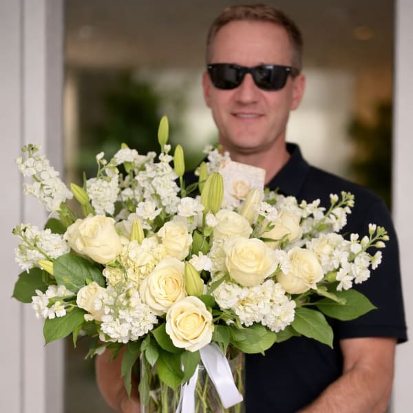 White roses and lilies arranged in a clear glass vase with a white ribbon