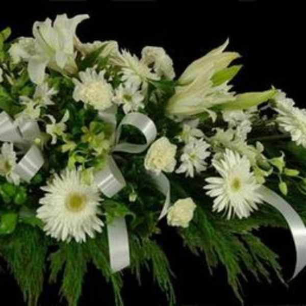 White floral casket spray with lilies, daisies, and ribbon accents