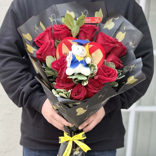 Bouquet of red roses with a small teddy bear in graduation attire