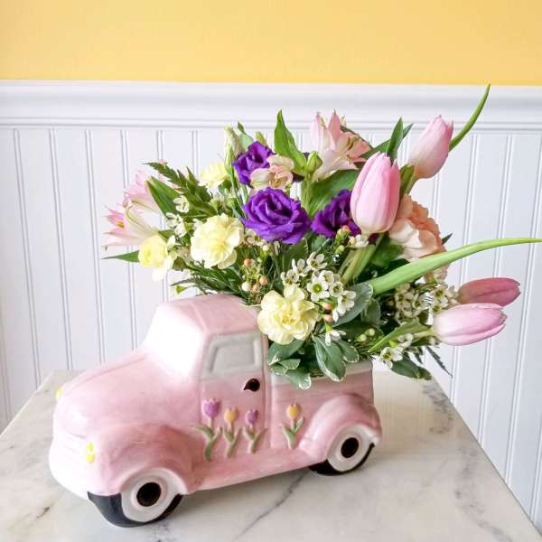 Pink tulips and mixed flowers arranged in a pink ceramic truck planter