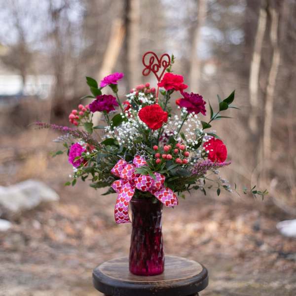 Pink and red carnation bouquet in a glass vase with a heart ribbon