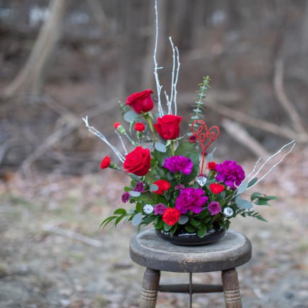 Red roses and purple flowers in a low black bowl with a "Love" pick