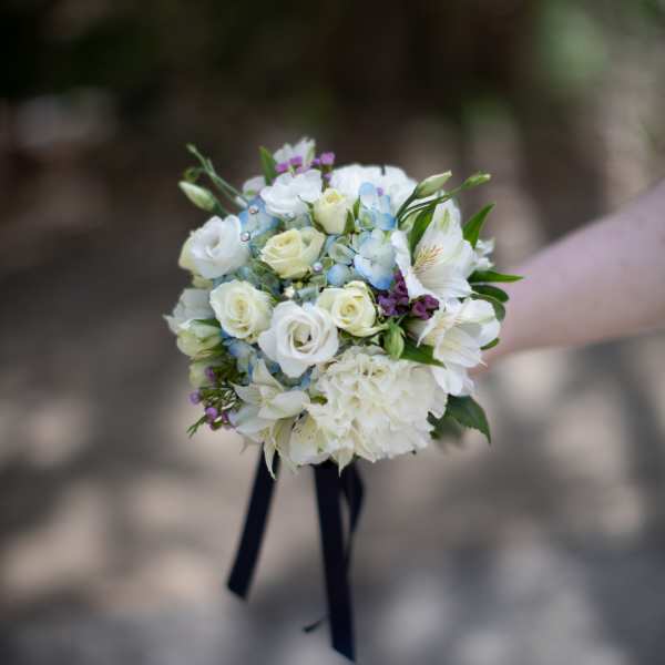 Handheld bouquet of white and pale blue flowers with dark ribbon tails