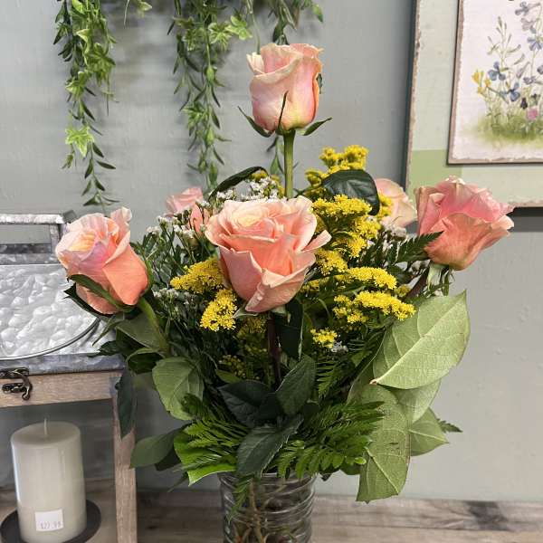 Pink roses arranged in a clear glass vase with yellow filler flowers