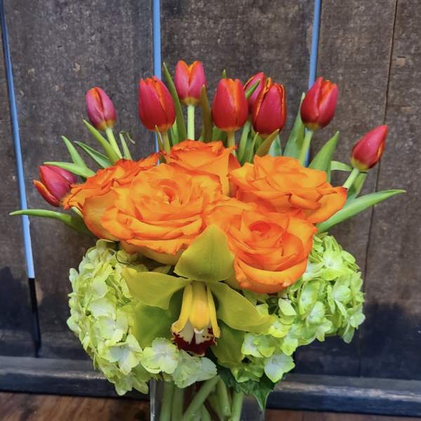 Orange roses and red tulips arranged in a clear glass vase