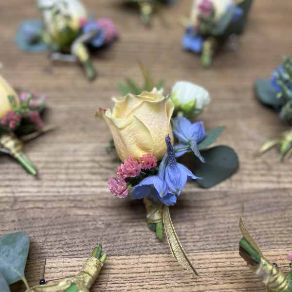 Small boutonniere with a cream rose and blue flowers on a wooden table