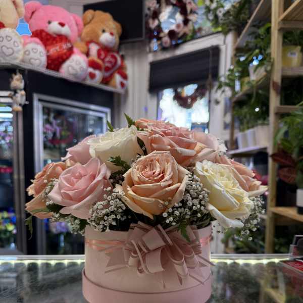 Pink and peach roses arranged in a round pink box with a ribbon bow