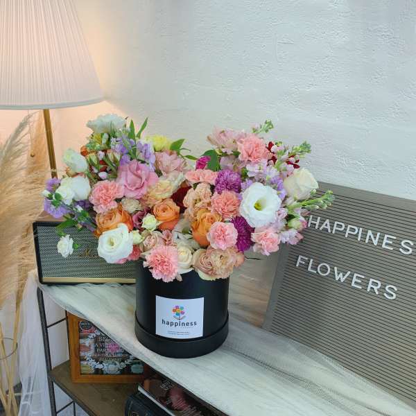 Mixed pastel flower arrangement in a black hatbox beside a lamp