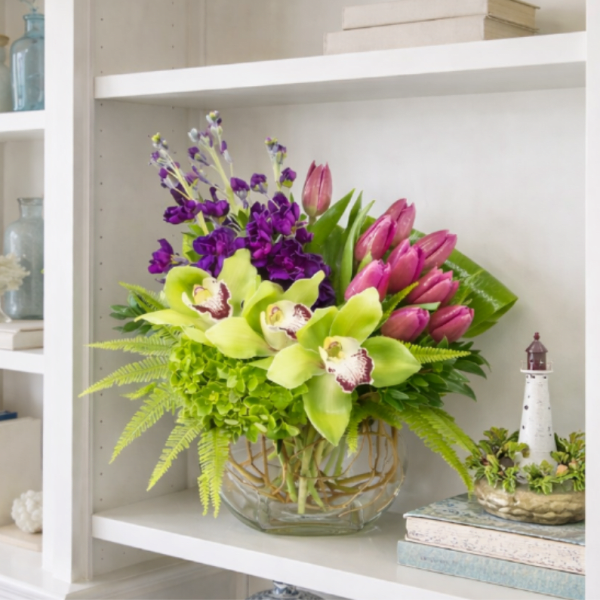 Bouquet of green orchids, pink tulips, and purple flowers in a glass vase