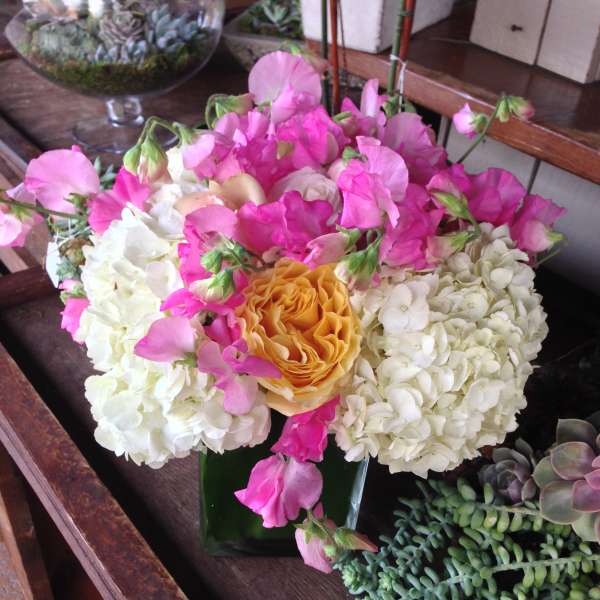 Pink sweet peas and white hydrangeas around a yellow rose in a glass vase