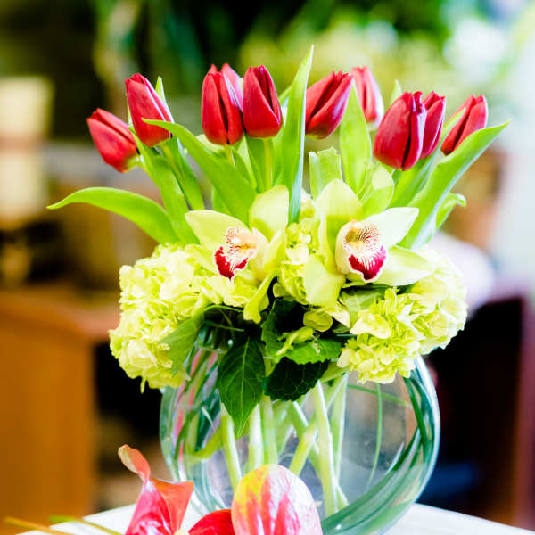 Red tulips and pale green orchids in a clear glass vase