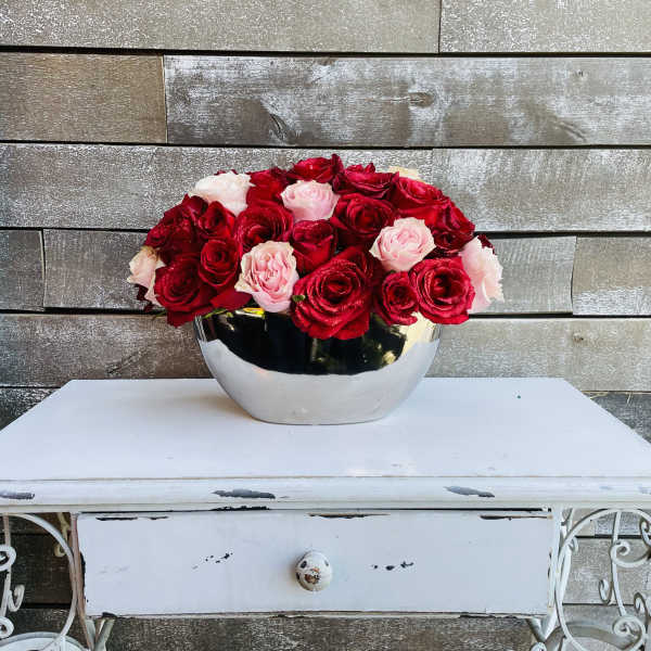 Red and blush roses arranged in a silver bowl on a white table